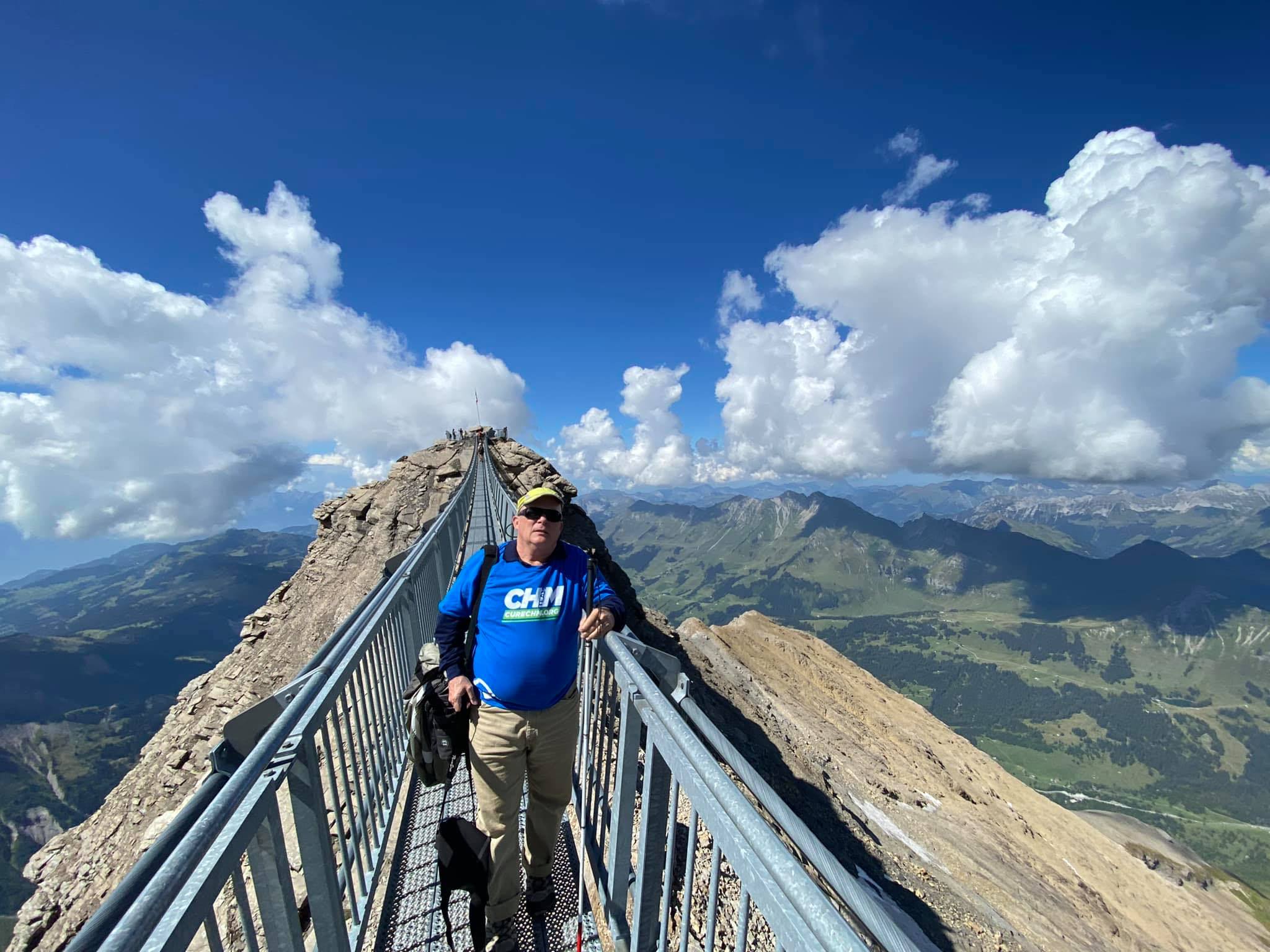 H. Eric Hartman, also known as the Blind/Low-Vision Traveler, stands on a bridge overlooking a mountain range.