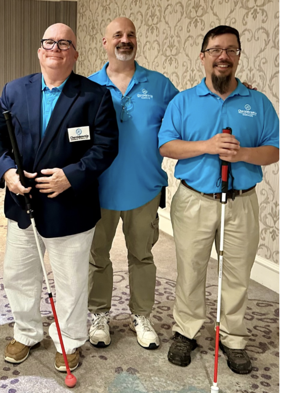 Three men with choroideremia standing side by side and smiling; two of the men are using white canes.