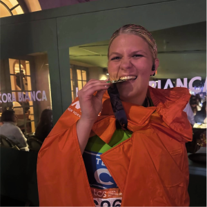 Team CHM runner Brooklynn Jenson biting her TCS New York City Marathon finisher medal.