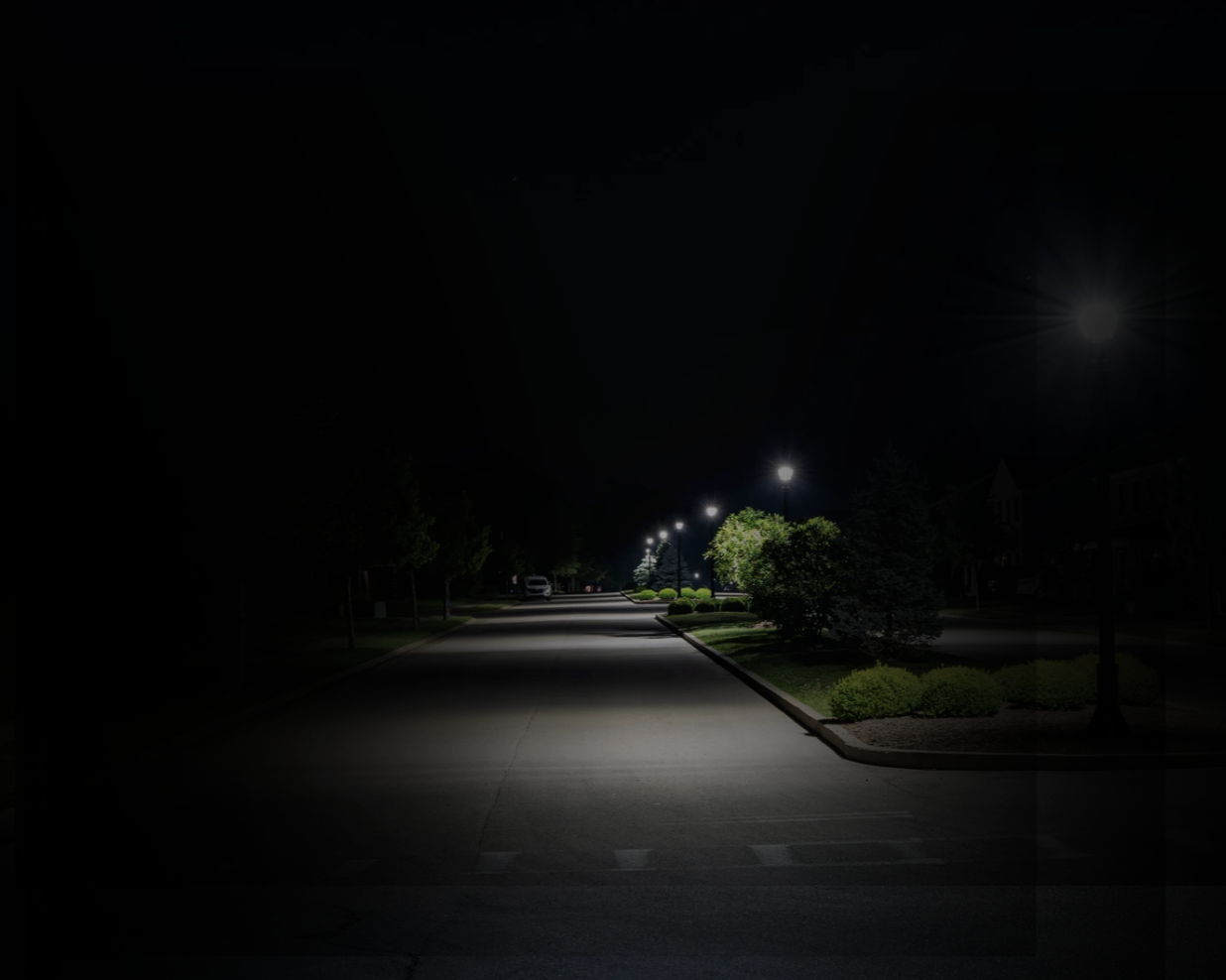 Same city street at night, but much of the scene is dark and details are obscured, illustrating how someone with choroideremia may experience reduced night vision and difficulty seeing in low light.